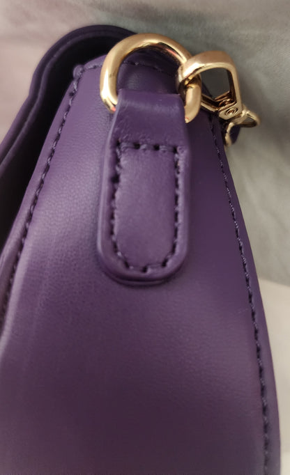 Close-up of the purple Taipei vegan leather shoulder purse showing a stitched tab, a gold-tone metal ring, and a gold lobster claw clasp for the removable shoulder strap on a soft light gray background.